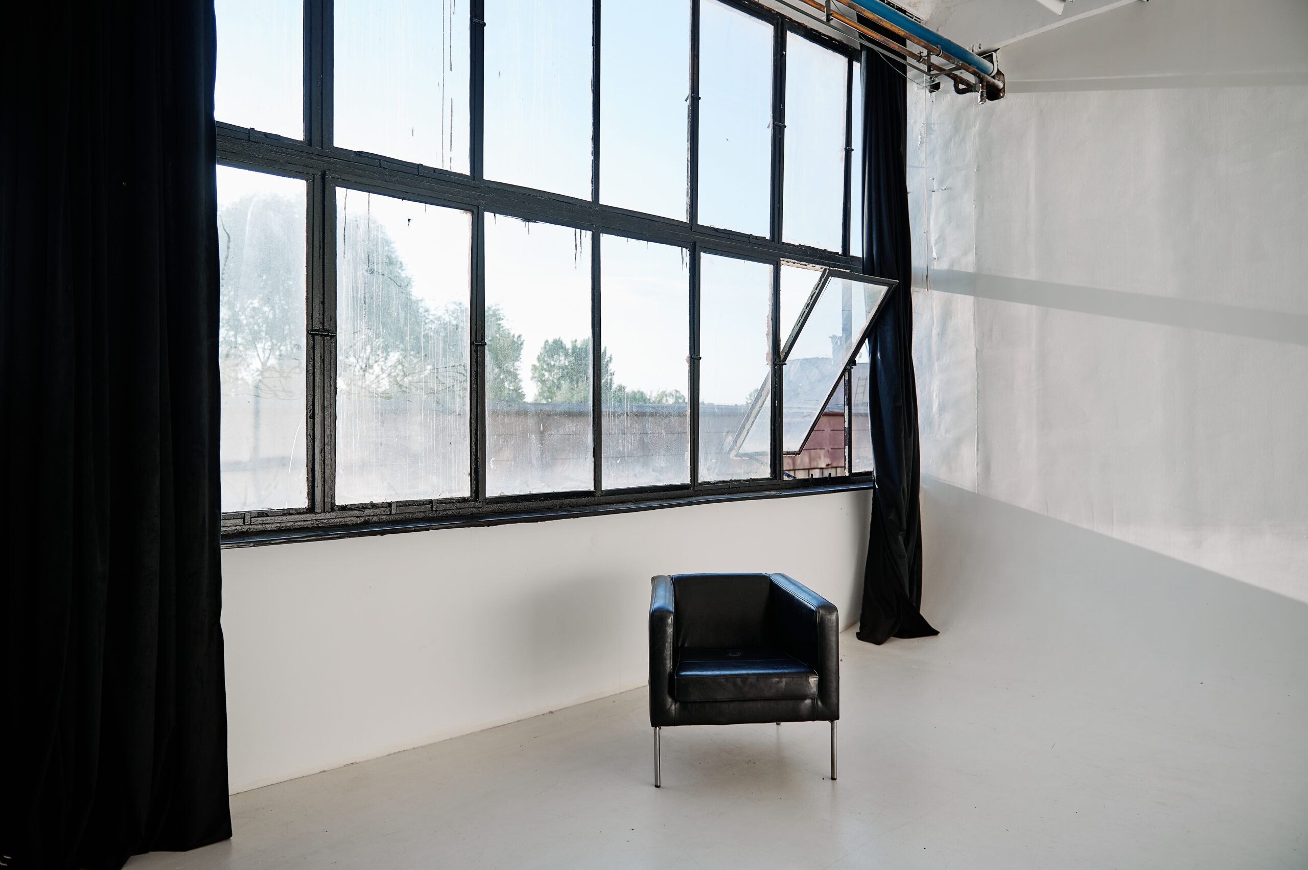 Czarny, skórzany fotel na tle ściany z czarnymi oknami w białej sali z cykloramą.
