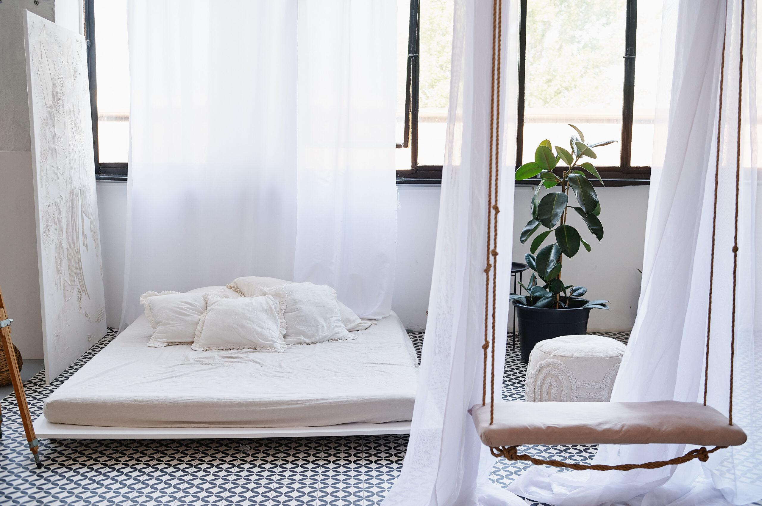 Wyposażenie sali LOFT - łóżko z białą pościelą na tle ściany z dużymi oknami, przed nim wisząca huśtawka.