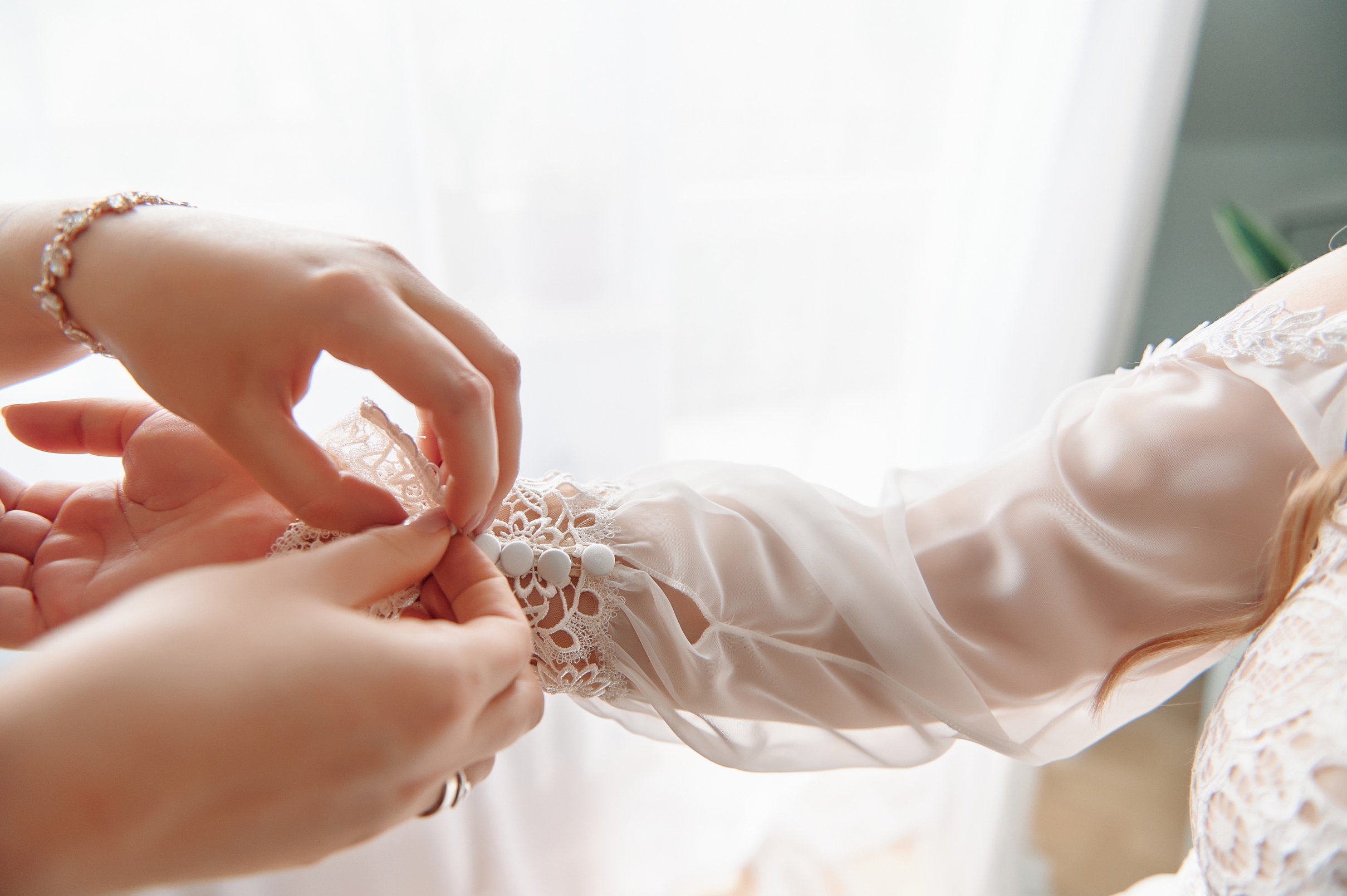 Kobiece dłonie zapinające guzik w rękawie sukni panny młodej.